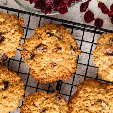 looking down on cranberry and oat cookies on a wire rack with a few cranberries spilling from a bowl.