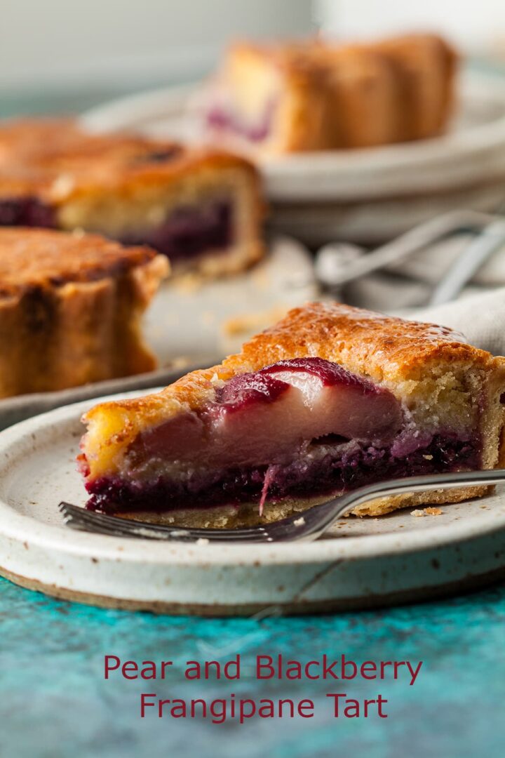 slice of pear and blackberry frangipane tart on plate with remaining tart behind.