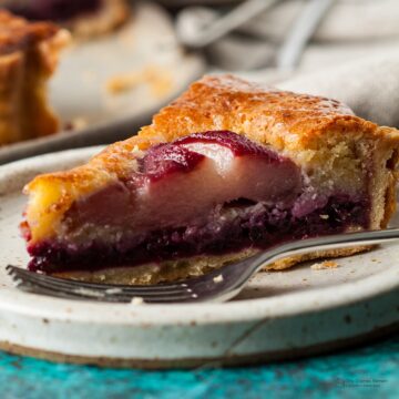 slice of pear and blackberry frangipane tart on a plate with a fork in front.