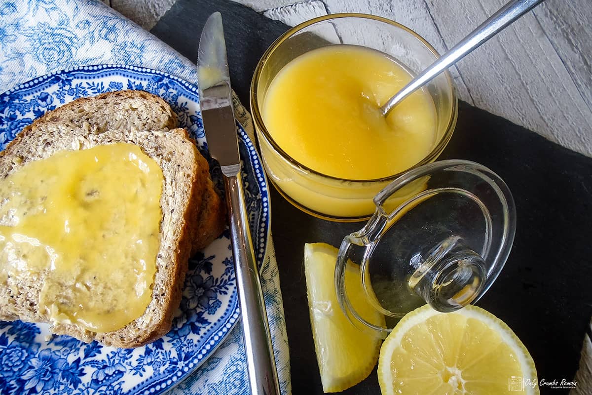 lemon curd in jar with bread spread with lemon curd to one side.