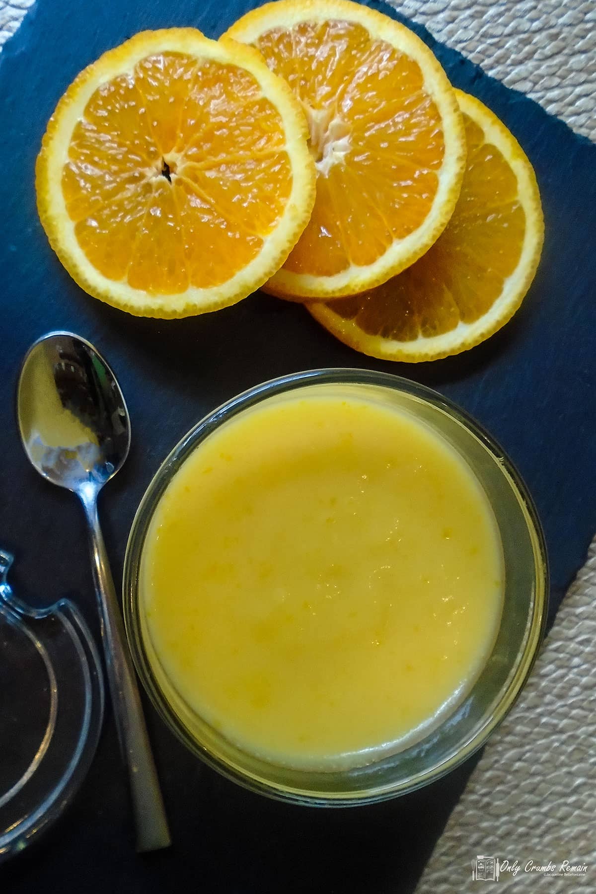 jar of homemade orange curd with spoon and sliced oranges.