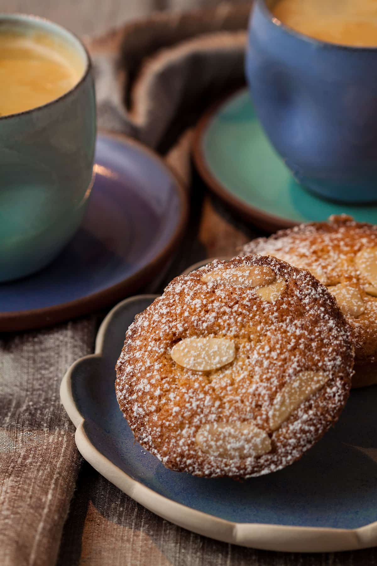 two frangipane mince pies on a plate with coffee cups behind.