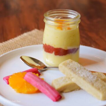 orange posset layered with rhubarb compote in glass jar served with shortbread orange slices and rhubarb batons.