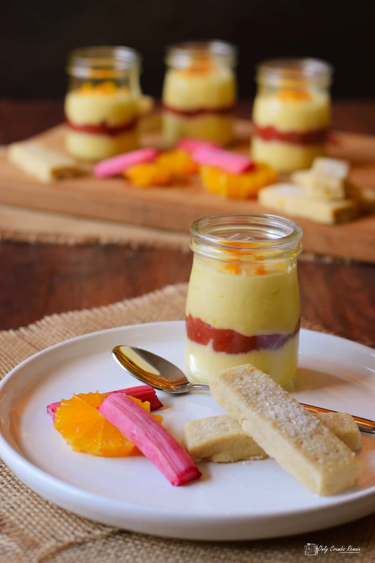 orange posset layered with rhubarb compote in glass jar served with shortbread orange slices and rhubarb batons.