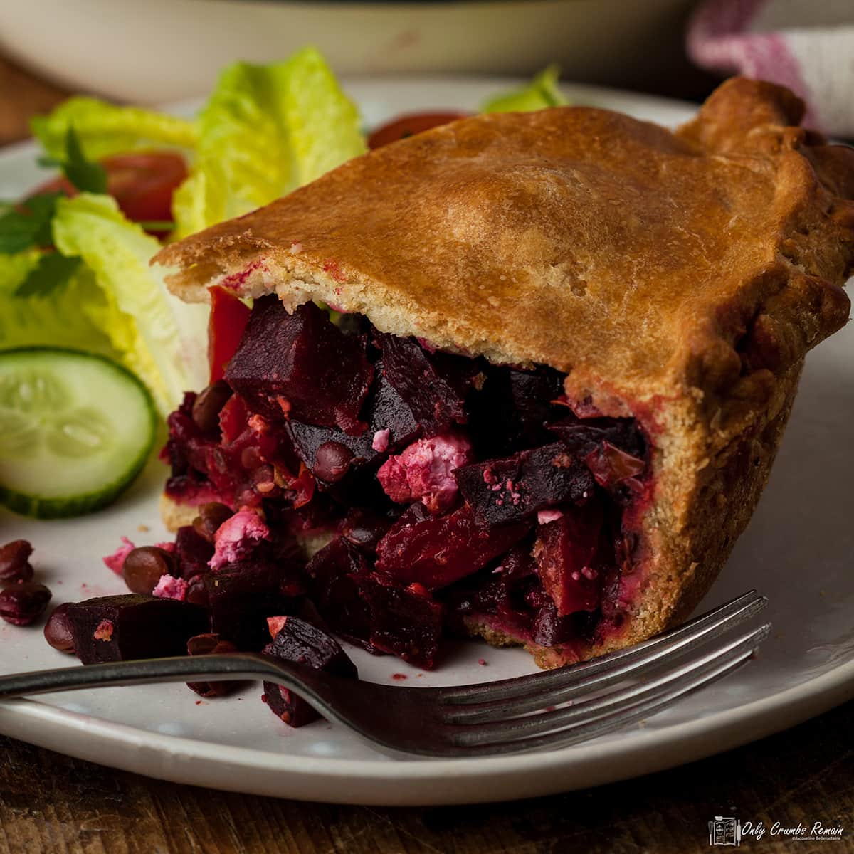 portion of beetroot and lentil vegan pie on a plate with fork in front and salad behind.