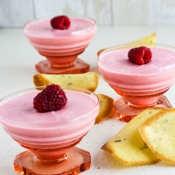 3 raspberry mousse in pink glass dishes with tuile biscuits on the side.