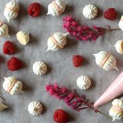 raspberry and white chocolate meringue kisses on baking parchment with piping bag and fresh raspberries