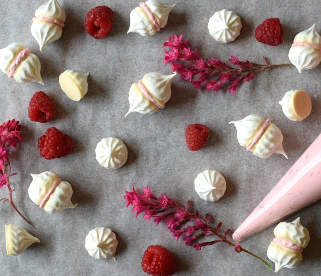 raspberry and white chocolate meringue kisses on baking parchment with piping bag and fresh raspberries
