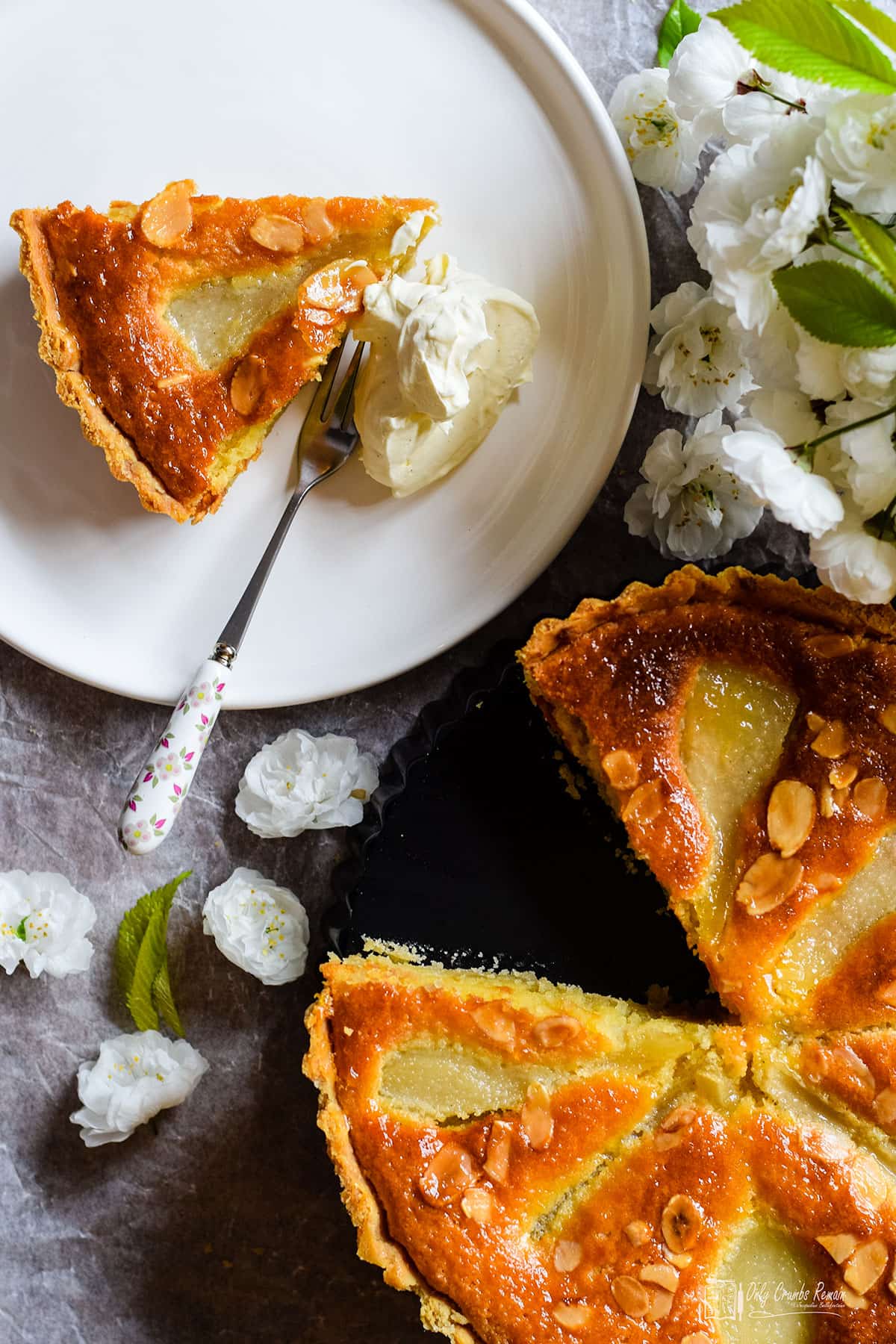 pear and almond tart with slice out on a plate served with a dollop of cream.