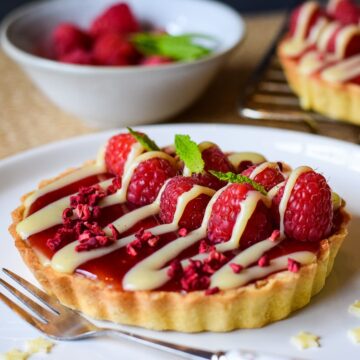 raspberry and white chocolate tart on serving plate with dessert fork on the side.
