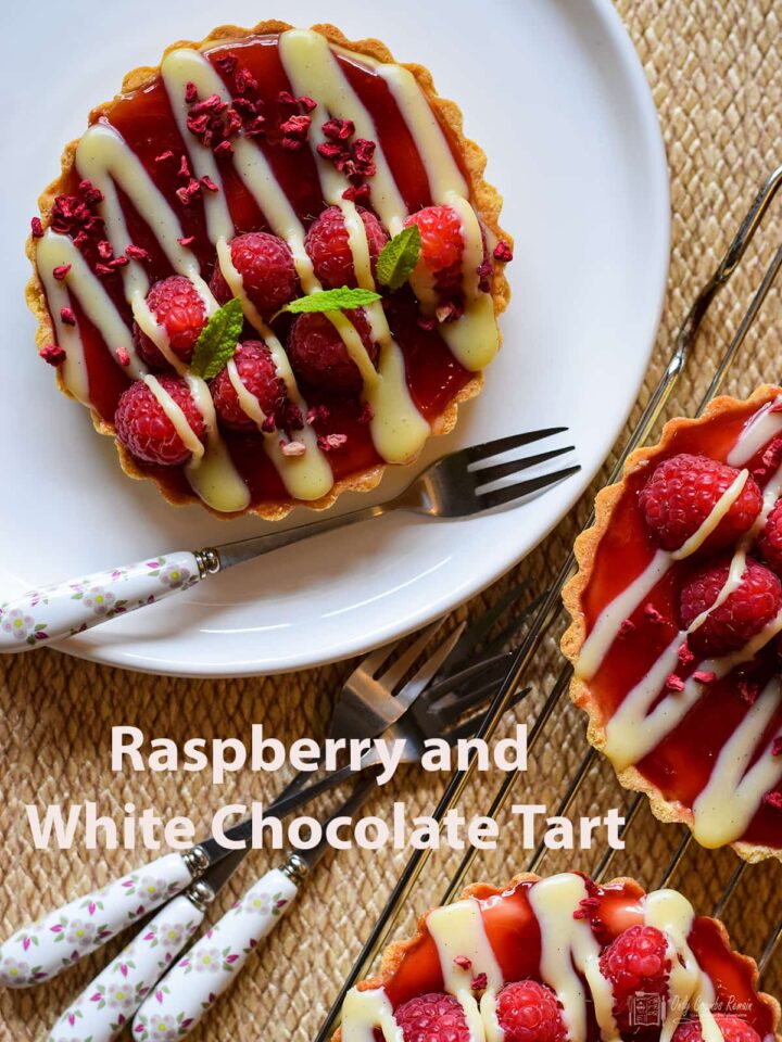raspberry and white chocolate tart on serving plate. Additonal tarts on cooling racl