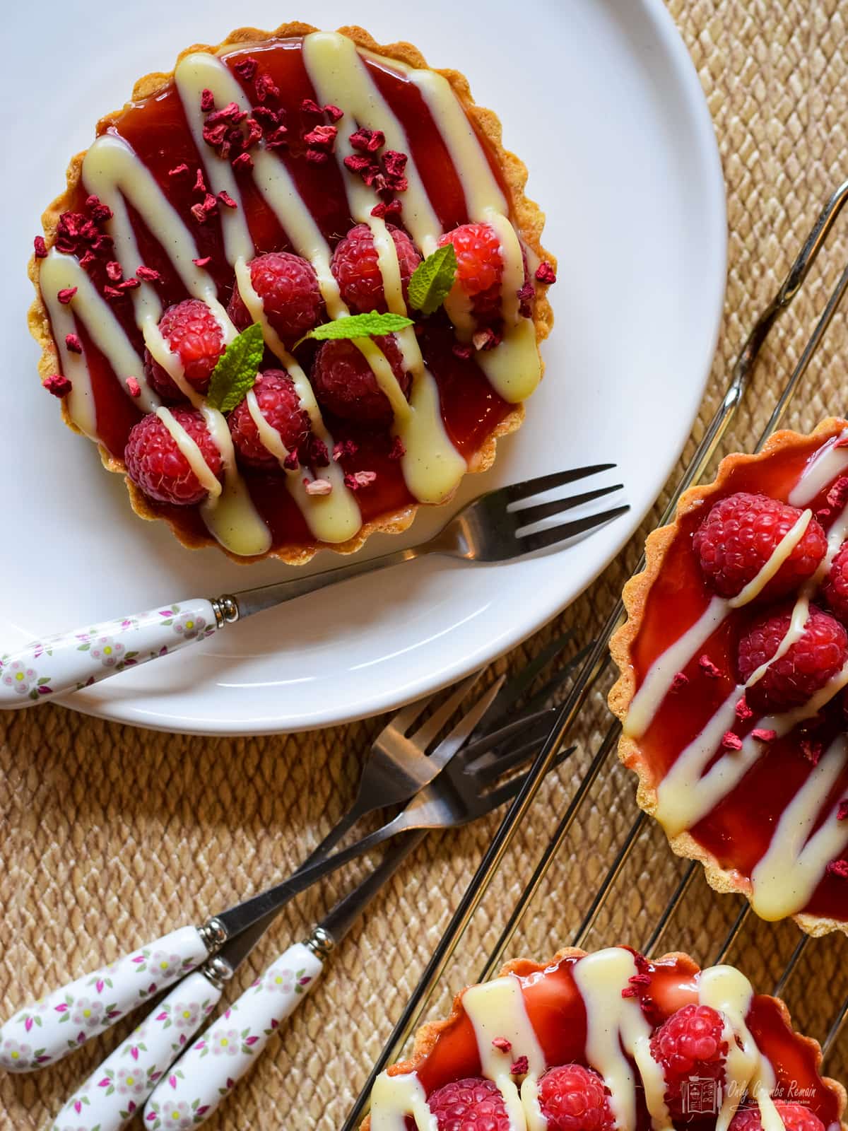 raspberry and white chocolate tart on a plate with dessert fork and two more tarts on cooling rack.