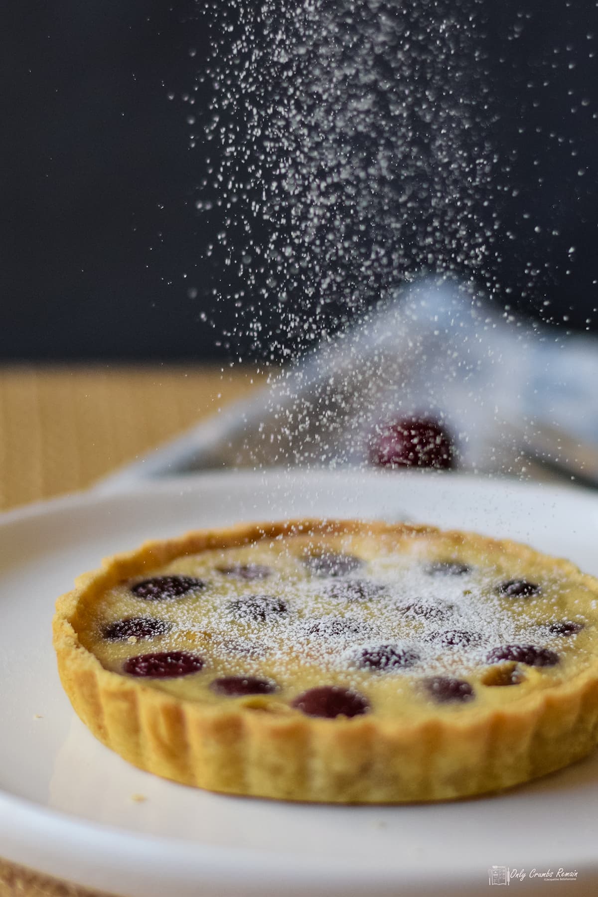 cherry clafoutis tart being dusted with icing sugar.