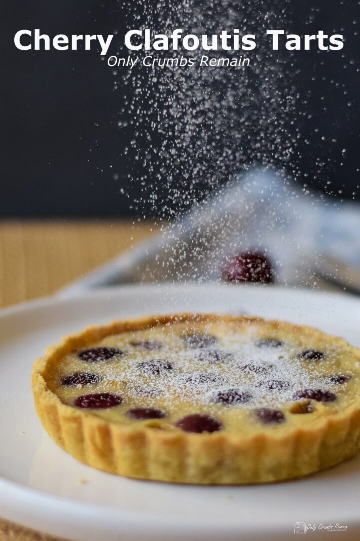 individual cherry clafoutis tart being dusted with icing sugar.