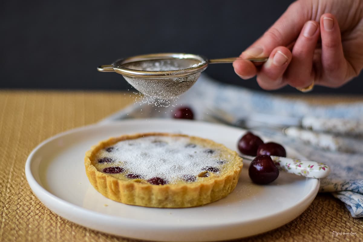 dusting a clafoutis tart with icing sugar.