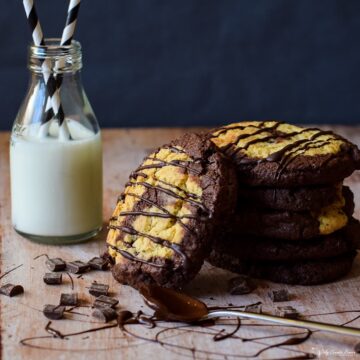 stack of triple chocolate orange pinwheel cookies by mini bottle of milk with chocolate chips and melted chocolate on a spoon in foreground.