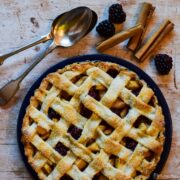 Spiced blackberry and pear lattice Pie in tin with spoons, blackberries and cinnamon sticks on the background.