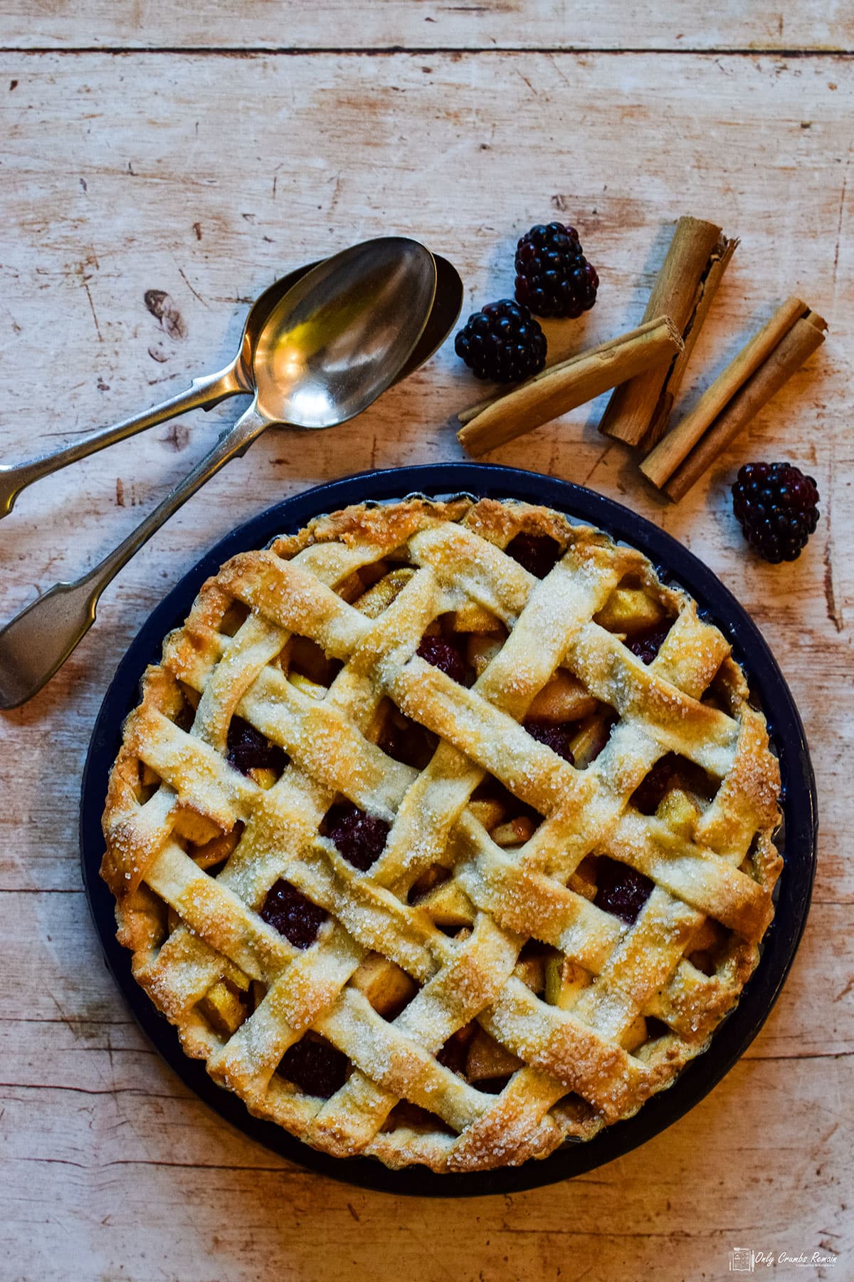 blackberry and pear lattice Pie in tin with spoons, blackberries and cinnamon sticks on the background.