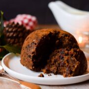 Chocolate orange Christmas pudding with slice of pudding laying on side on a serving plate.