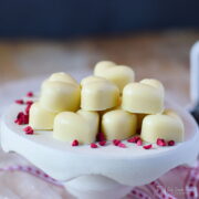 homemade raspberry cream white chocolates on a stand with freeze dried raspberries scattered around