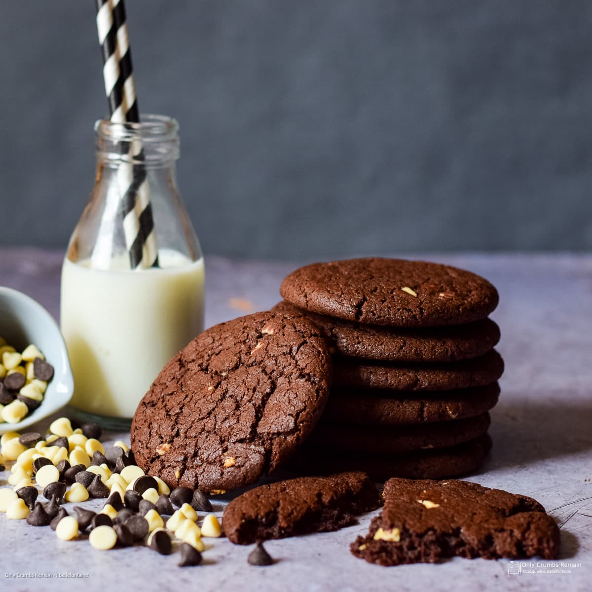 stack of easy double chocolate cookies beside a bottle of milk with 2 straws. On the other side a bow of chocolate chips spilling out in front of the milk and cookies.