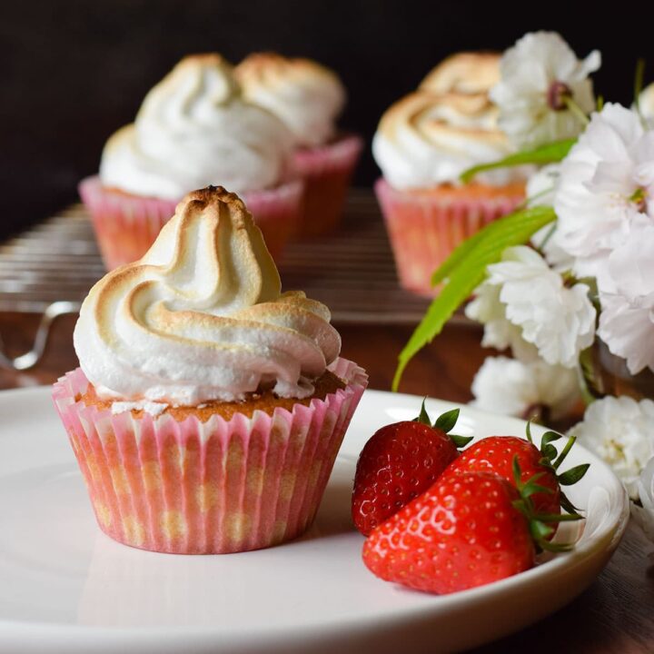 rhubarb and strawberry meringue cupcake on a plate with fresh strawberries.