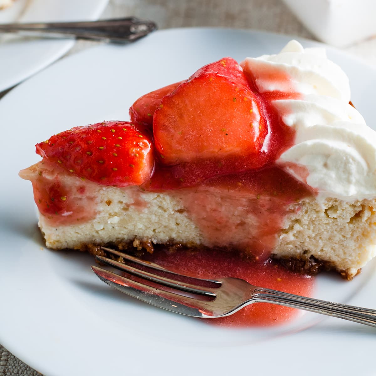 slice of baked strawberry cheesecake on white late with dessert fork.