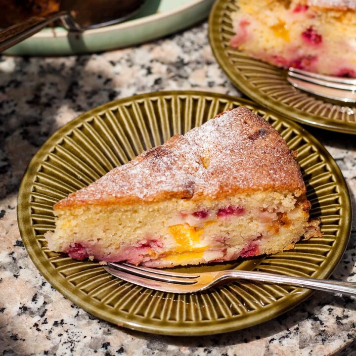 slice of easy peach and redcurrant cake on green plate with a pastry fork.