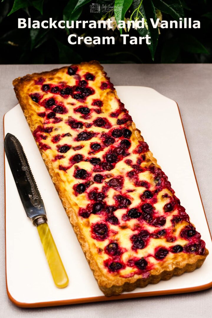 whole blackcurrant and vanilla cream tart on platter with knife beside.