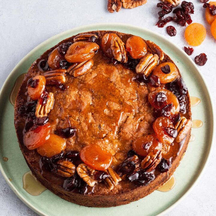 apricot cranberry and pecan fruit cake on green plate with dried fruit around.