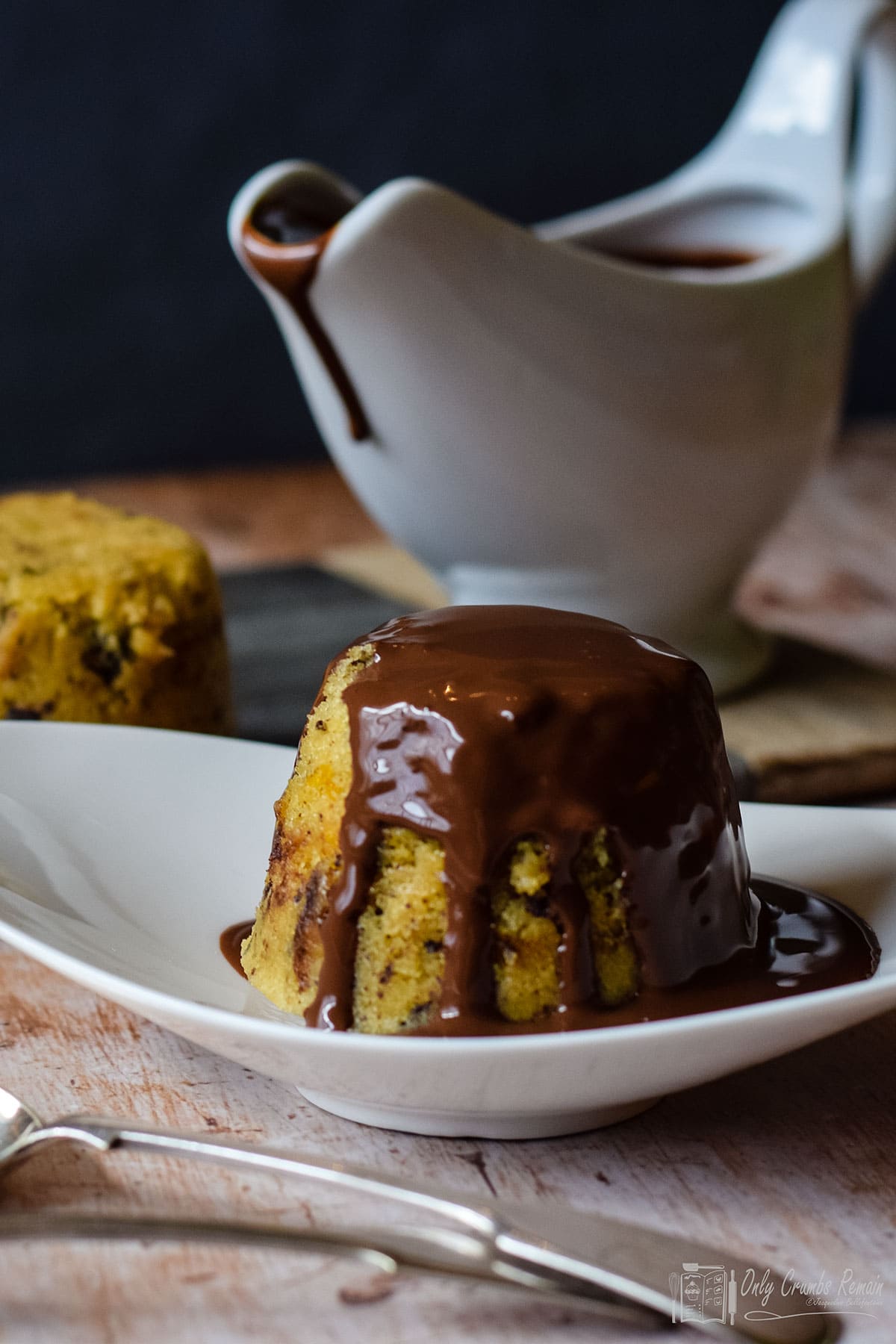 chocolate orange steamed pudding on a plate with jug of sauce behind.
