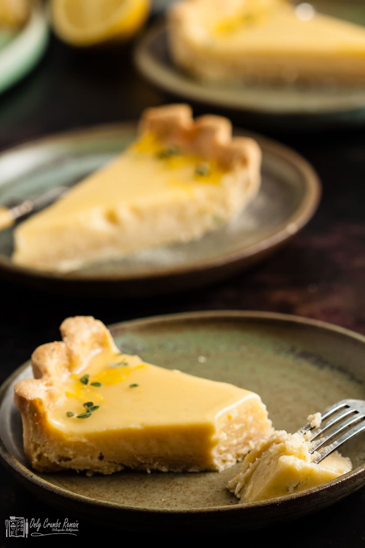 slices of lemon and gin tart on teaplates with portion removed with a fork on front plate.
