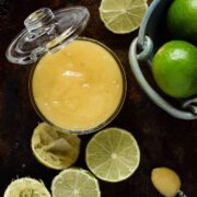jar of lime curd with whole, sliced and squeezes lemons on the side.