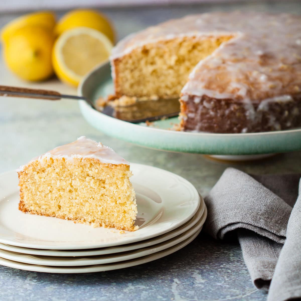 slice of lemon drizzle olive oil cake on a plate with remaining cake behind.