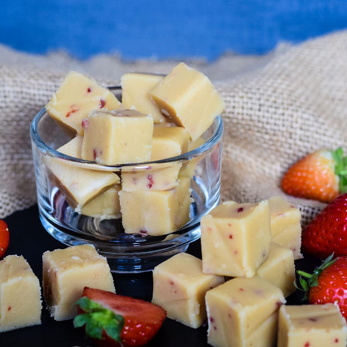 bowl of strawberry and vanilla fudge with some on a board and fresh strawberries.