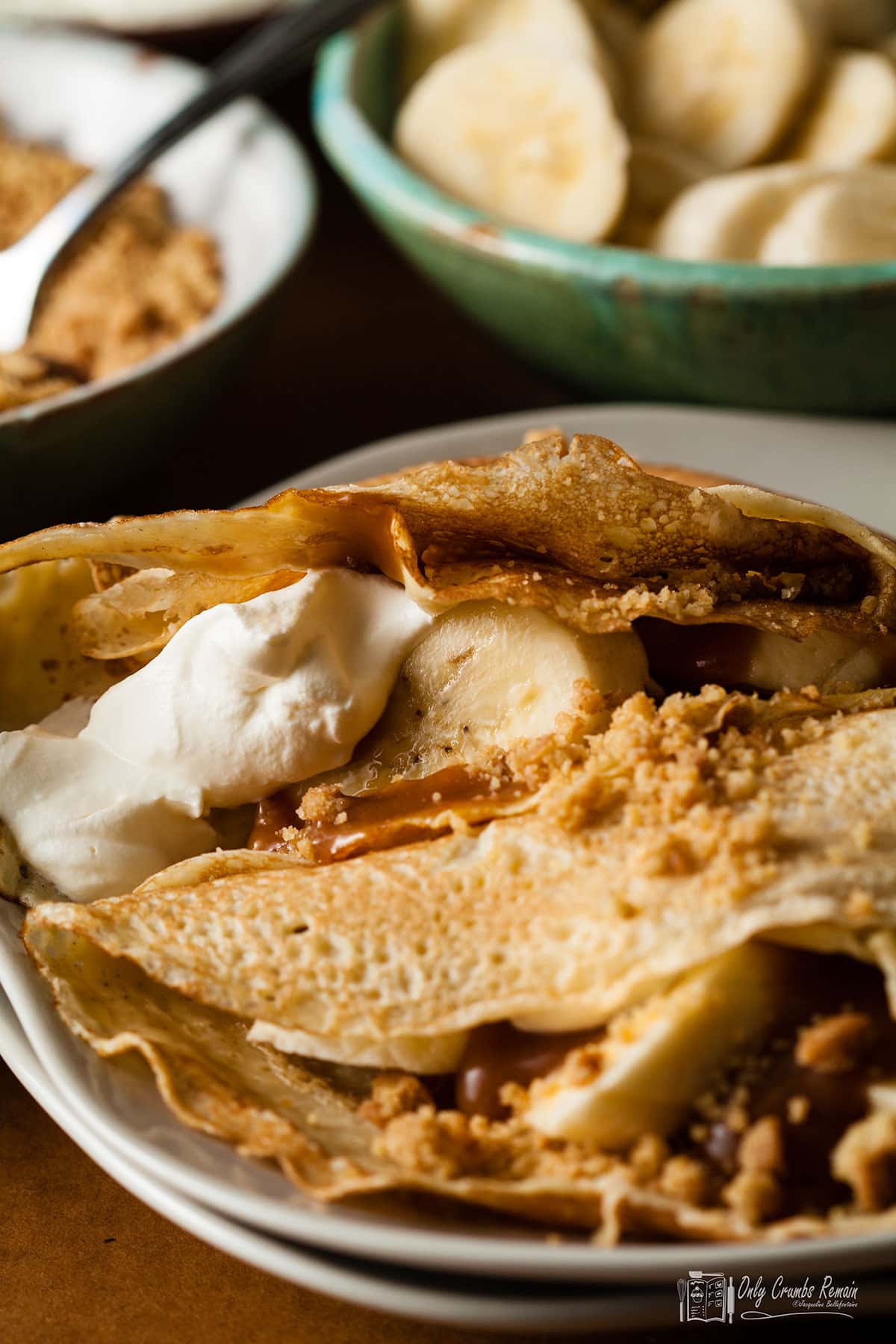 banoffee panackes on serving plate with bowls of crumbs and banana slices behind.