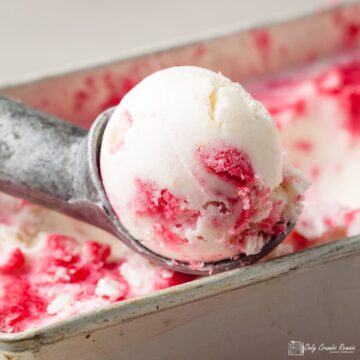 scoop of mascarpone and redcurrant ripple ice cream resting on container of ice cream.