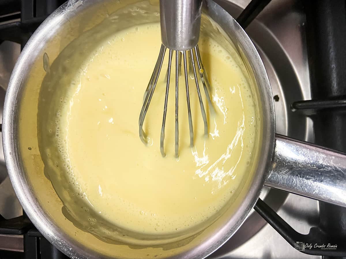thickened creme patisserie in a saucepan with whisk.