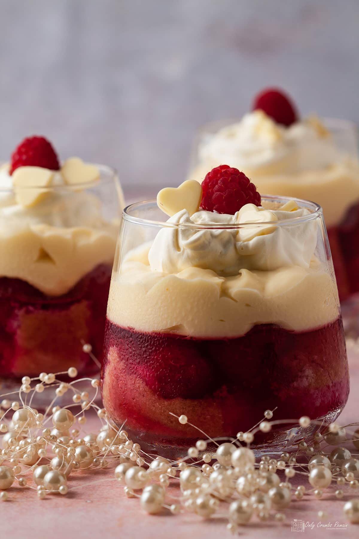 3 mini raspberry and white chocolate trifle in glasses with beads around the base of glass.