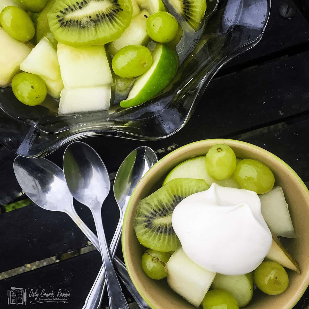 serving bowl and serving of green fruit salad with spoons on the side.