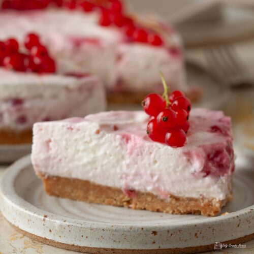 slice of redcurrant cheesecake on tea plate with remaining cake behind.