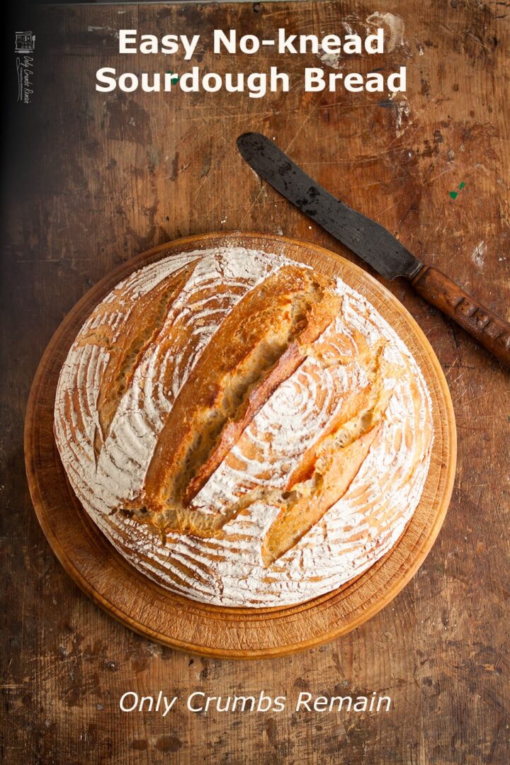 Whole round sourdough loaf on bread board with old bread knife to side.