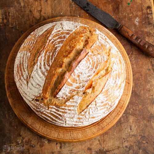 easy no knead sourdough loaf on a bread board with bread knife on the side.