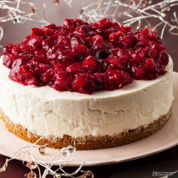 Cranberry and white chocolate cheesecake on pink plate with festive lights behind.