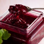 spoon lifting blackcurrant and raspberry compote out of a jar.