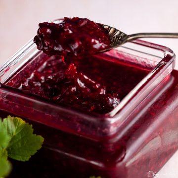 spoon lifting blackcurrant and raspberry compote out of a jar.