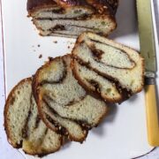 Cinnamon and hazelnut babka on a white board sliced to reveal the marbling effect.