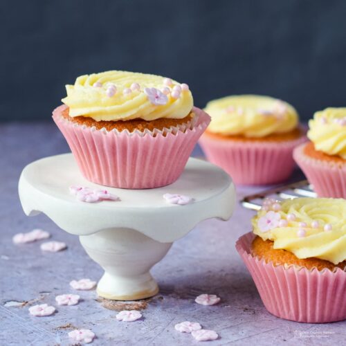 lemon and elderflower cupcake on mini cake stand with more cupcakes behind.