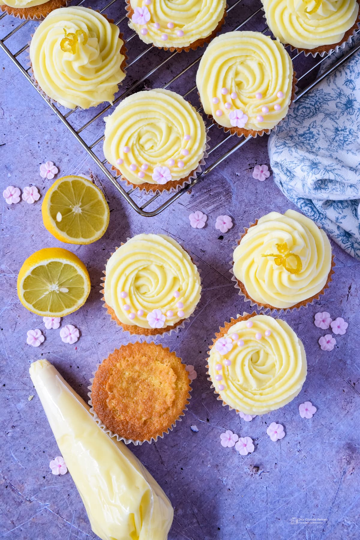 lemon and elderflower cupcakes on a cooling rack with part finished cake on work surface along with piping bag