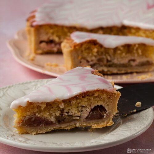 portion of Rhubarb Bakewell Tart on a plate with cut tart on serving plate behind.